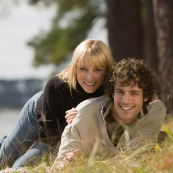 Smiling couple lying together on the grass in a relaxed outdoor setting, symbolizing trust, openness, and connection in the swinging lifestyle.