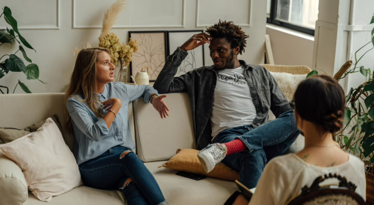Couple sitting together on a couch having an open, emotional talk with a counselor, symbolizing trust and honest swinger communication.