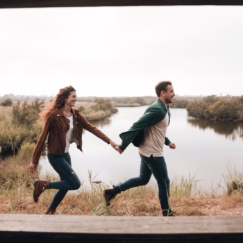 A couple holding hands by the water at sunset, symbolizing emotional connection and different swinger needs in a relationship.