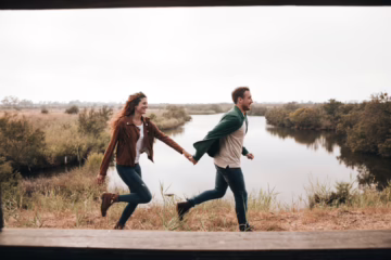 A couple holding hands by the water at sunset, symbolizing emotional connection and different swinger needs in a relationship.
