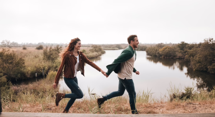 A couple holding hands by the water at sunset, symbolizing emotional connection and different swinger needs in a relationship.