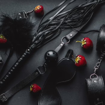 BDSM accessories and strawberries arranged on a dark background representing fetish party aesthetics and sensual play.