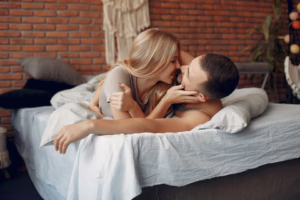 A couple cuddling and kissing in bed, showing emotional closeness before discussing different swinger needs and desires.