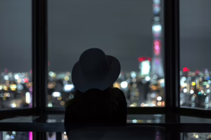 Silhouette of a woman in a hat looking out over a city at night, symbolizing desire, contemplation, and the emotional side of the cuckqueen dynamic