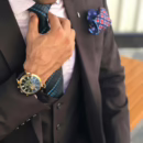 A close-up of a well-dressed man adjusting his tie, wearing an elegant watch and pocket square, symbolizing masculine confidence, desire, and refined HotHusband energy.