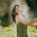 Woman laughing while opening a champagne bottle outdoors, symbolizing release, joy, and sexual awakening in a real erotic story about first time squirting.