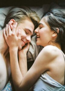 Couple lying close together and smiling during an intimate moment, representing trust and emotional connection in swinger couple goals.