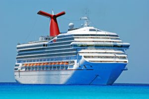 White Carnival cruise ship sailing through bright turquoise ocean waters under a clear blue sky during daytime.