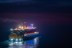 Luxury cruise liner glowing with colorful lights while traveling across dark ocean waters at night, creating a romantic and adventurous atmosphere.