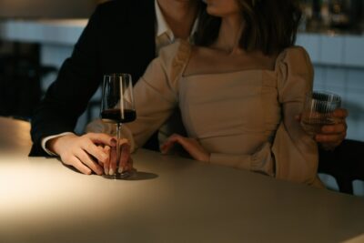 A stylish couple enjoys wine at a softly lit bar, reflecting the anticipation and excitement before meeting another couple for the first time.
