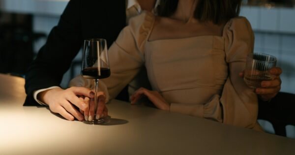 A stylish couple enjoys wine at a softly lit bar, reflecting the anticipation and excitement before meeting another couple for the first time.