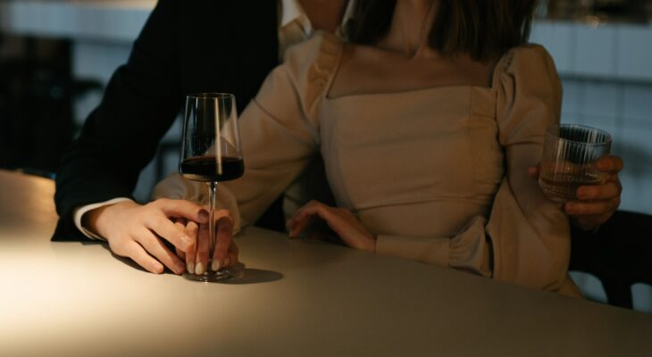 A stylish couple enjoys wine at a softly lit bar, reflecting the anticipation and excitement before meeting another couple for the first time.