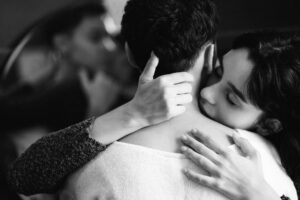 A woman embraces and kisses a man's neck while another couple shares an intimate moment in the background, capturing the emotional connection and atmosphere of a consensual partner swap.