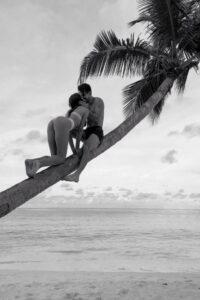 Couple sharing an intimate kiss on a leaning palm tree, illustrating the playful chemistry and attraction many couples experience on holiday.