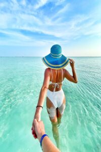 Couple walking hand in hand into crystal-clear tropical water, capturing the excitement, connection, and romance that often spark vacation libido.